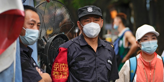 On Tuesday, July 19, 2022, a security guard wearing a face mask is standing at South Luogu Lane, a popular tourist attraction in Beijing. 