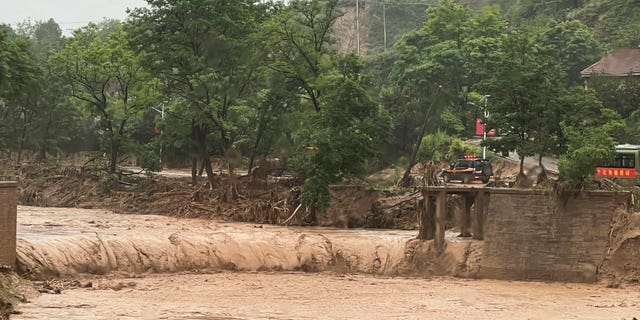 A vehicle is seen near a part of a bridge that was washed away by flood waters along a river in Qingyang in northwest China's Gansu province Saturday, July 16, 2022. Flash floods in southwest and northwest China have left at least a dozen dead and put thousands of others in harm's way, state media reported Sunday. 