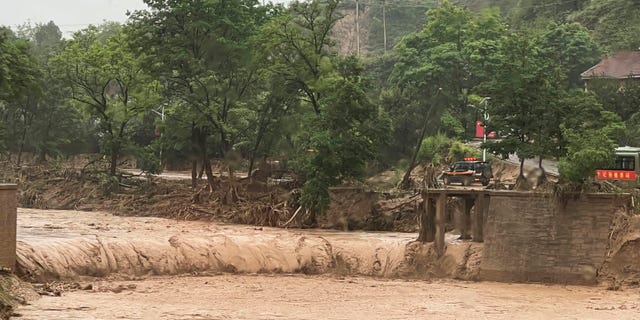 A car is seen near part of a bridge that was washed away by flood waters along a river in Qingyang in northwest China's Gansu province on Saturday, July 16, 2022. thousands more are at risk, state media reported on Sunday.