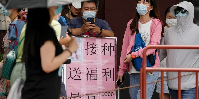 Residents wearing face masks walk by a poster that reads, "Vaccination free benefits up to 1,000 yuan" in Beijing, Tuesday, July 19, 2022.