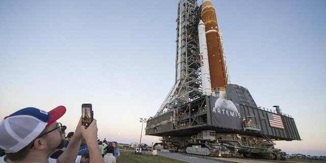 Des invités et des employés de la NASA prennent des photos alors que la fusée Space Launch System (SLS) de la NASA avec le vaisseau spatial Orion à bord roule pour la première fois depuis High Bay 3 du Vehicle Assembly Building, au Kennedy Space Center à Cape Canaveral, en Floride.