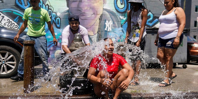 Jennifer Pagan, center, reacts as she sits in front of an open fire hydrant in The Bronx section of New York, Friday, July 22, 2022.