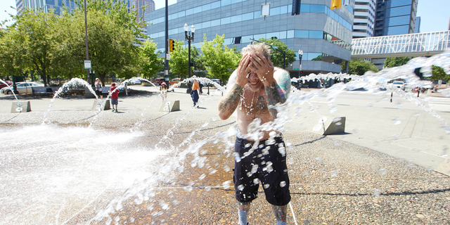 Matthew Carr cools off in the Salmon Street Springs fountain before returning to work cleaning up trash on his bicycle in Portland, Oregon, on Tuesday.