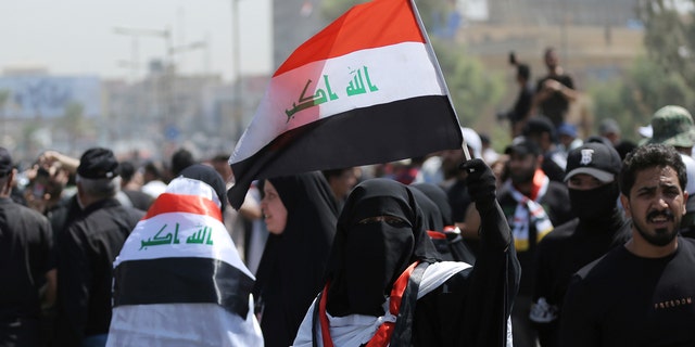 A veiled protester holds an Iraqi flag as people gather near the Green Zone area in Baghdad, Iraq on Saturday, July 30, 2022.