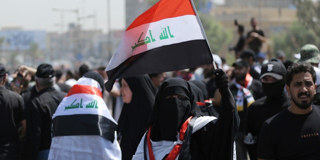 A veiled protester holds an Iraqi flag as people gather near the Green Zone area in Baghdad, Iraq on Saturday, July 30, 2022.