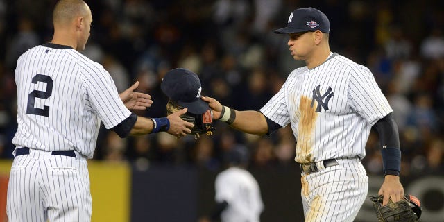 Alex Rodriguez, #13 of the New York Yankees, hands Derek Jeter, #2, his baseball hat and glove during Game One of the American League Championship Series against the Detroit Tigers at Yankee Stadium on October 13, 2012 in the Bronx borough of New York City, New York. The Tigers defeated the Yankees 6-4 in 12 innings.