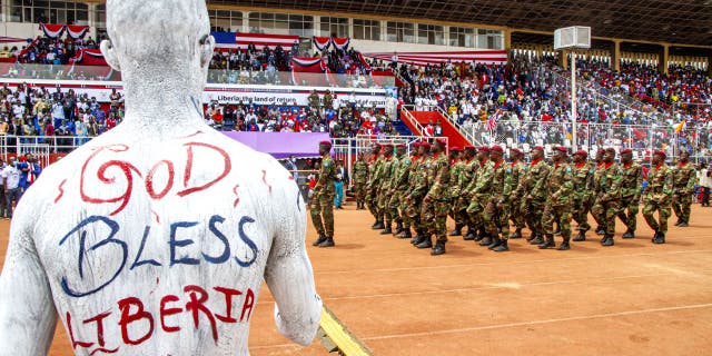 A Liberian artist paints his shirt with the national colours and the words 'God Bless Liberia' on his back during the military parade at the Liberia Bicentennial Celebration on February 14, 2022, in Monrovia