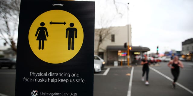 People jog past a social distancing sign on the first day of New Zealand's new coronavirus disease (COVID-19) safety measure, which requires masks to be worn on public transport, in Auckland, New Zealand, August 1.  31st, 2020.  