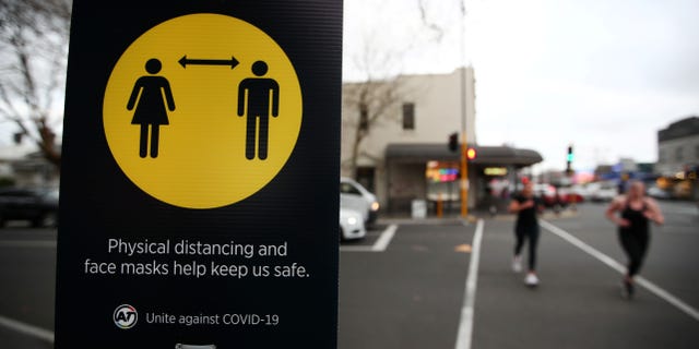 People jog past a social distancing sign on the first day of New Zealand's new coronavirus disease (COVID-19) safety measure that mandates wearing of a mask on public transport, in Auckland, New Zealand, on Aug. 31, 2020.