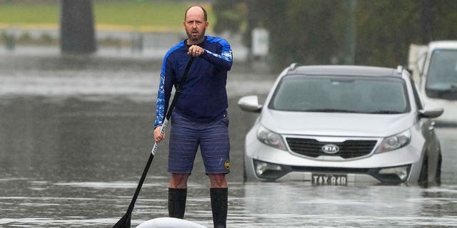 A man paddles on a stand-up paddle board through a flooded street at Windsor on the outskirts of Sydney, Australia, Tuesday, July 5, 2022. Hundreds of homes have been inundated in and around Australia's largest city in a flood emergency that was impacting 50,000 people, officials said Tuesday. 