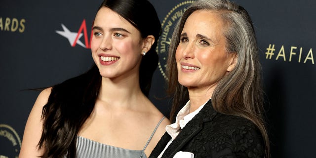 Margaret Qualley wears a grey dress on the red carpet with long dark hair next to mother Andie MacDowell in a dark suit