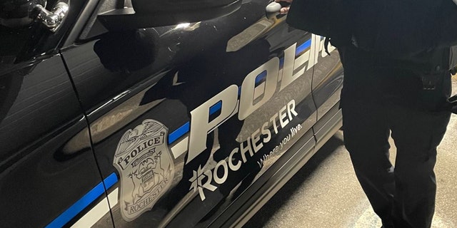 An officer stands next to a Rochester Police Department patrol car.