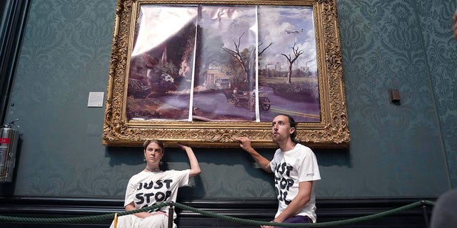 Protesters glue their hands to the frame of John Constable's The Hay Wain after first having covered the painting with their own picture, inside the National Gallery, London, Monday July 4, 2022. Police say two climate change protesters have been arrested after they glued themselves to the frame of a famous John Constable painting hanging in Britain’s National Gallery. The two, from the protest group "Just Stop Oil," stepped over a rope barrier and covered "The Hay Wain" on Monday with large sheets of paper depicting "an apocalyptic vision of the future" of the landscape. 