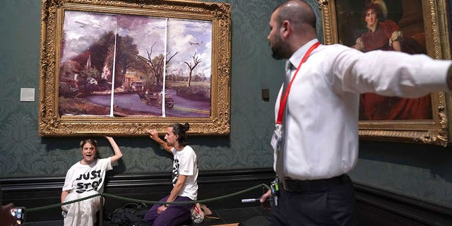 A security guard looks at protesters who glued their hands to the frame of John Constable's The Hay Wain, inside the National Gallery, London, Monday July 4, 2022. 