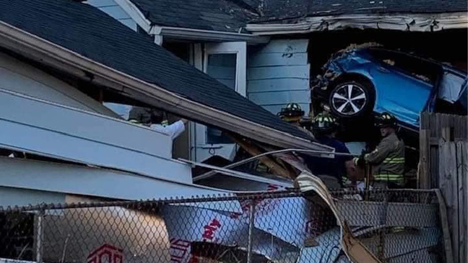 A blue SUV is seen sticking out of a home following a crash