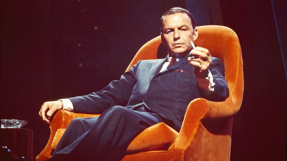 Frank Sinatra sitting in an orange chair with a cigarette in hand in 1955.