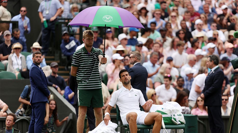 Novak Djokovic sits under umbrella during break