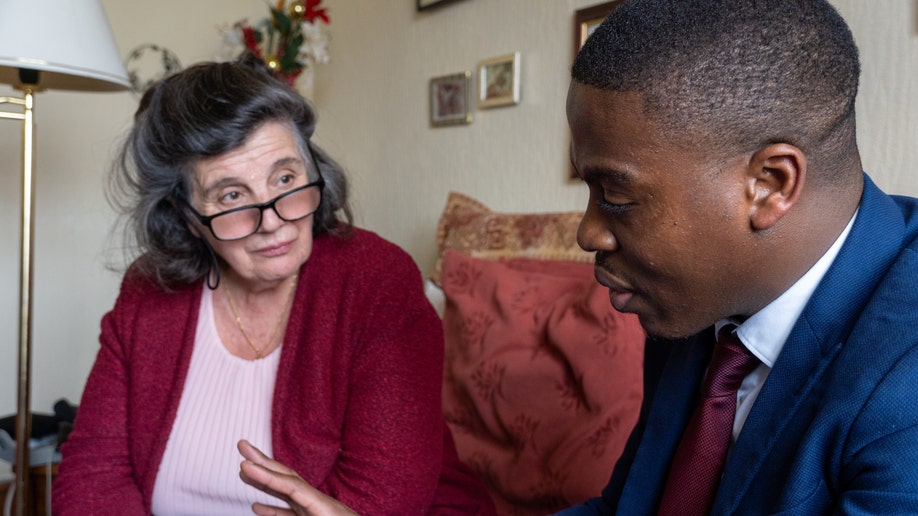 Rosa Lalor, an elderly British woman in glasses speaks with younger Black man in a suit