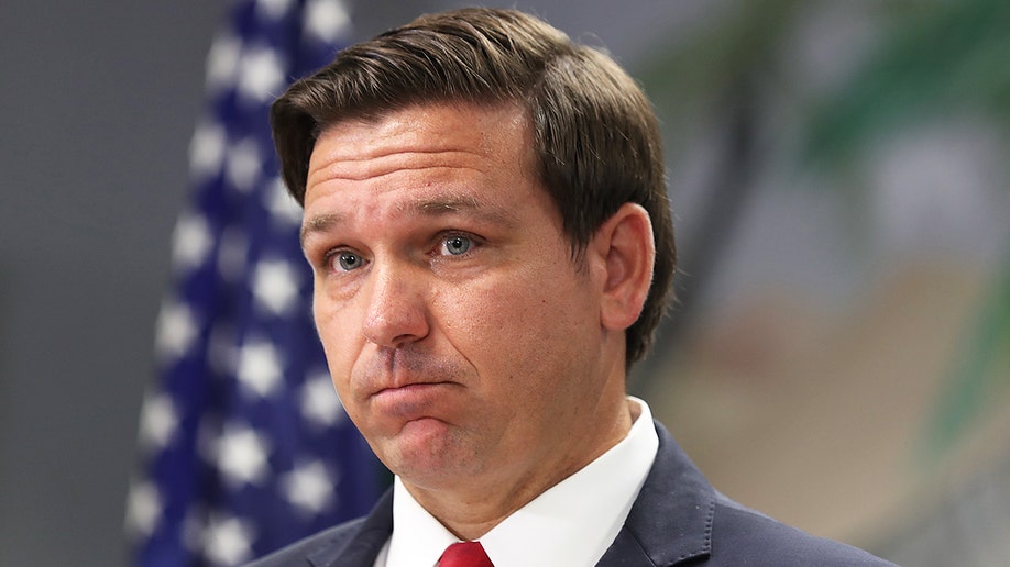 Ron DeSantis of Florida with American flag behind in a suit and tie
