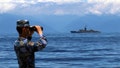 A People's Liberation Army member looks through binoculars during military exercises as Taiwan&rsquo;s frigate Lan Yang is seen at the rear, on Friday, Aug. 5, 2022. China has repeatedly entered the waters and airspace of Taiwan in the past several weeks, Taiwan defense officials have said.