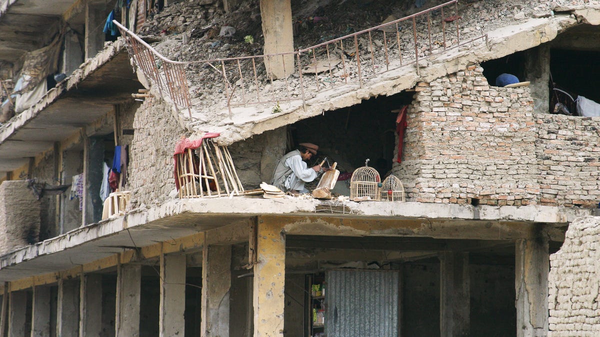 Afghan man sits in a destroyed brick building