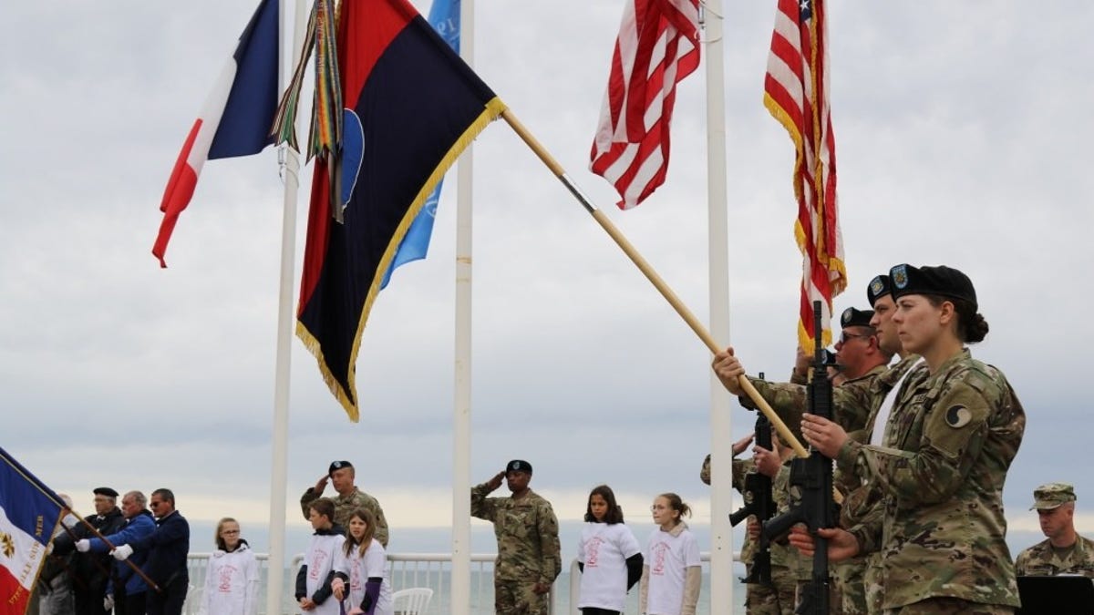 Army national guard members hold flag during D-Day ceremony