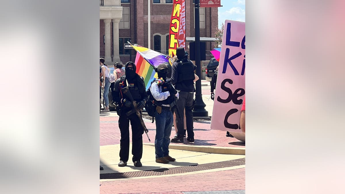 Masked black-clad Antifa protesters at drag brunch in Texas, holding an LGBTQ rainbow flag