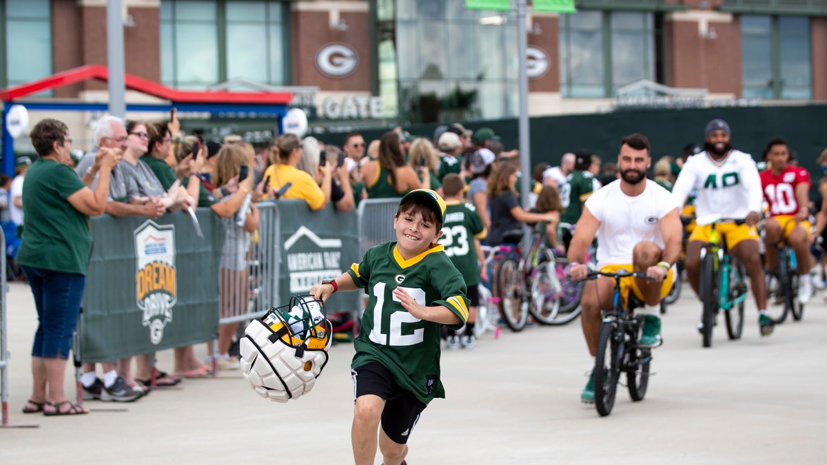 Green Bay Packers tight end Josiah Deguara, third from right, rides a young fan's bike as the fan takes off running with Deguara's helmet 