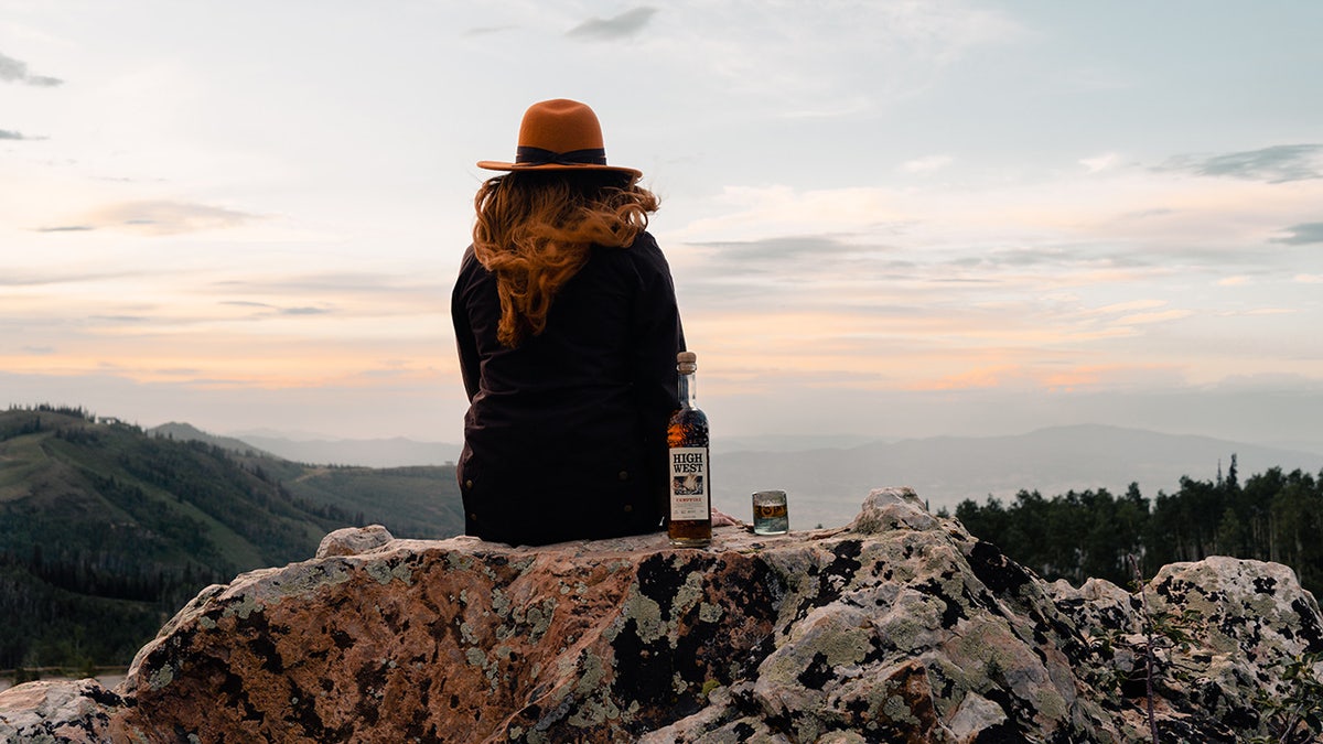 woman on mountain with campfire whiskey