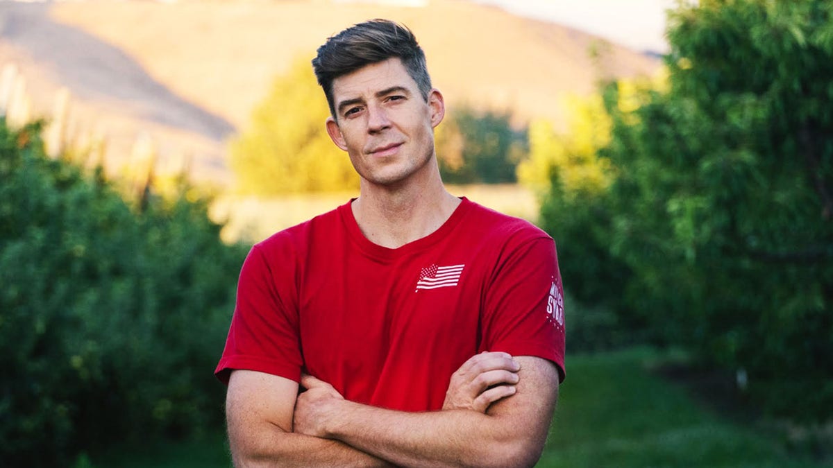 Corey Gibson wearing a red shirt posing for a picture outside