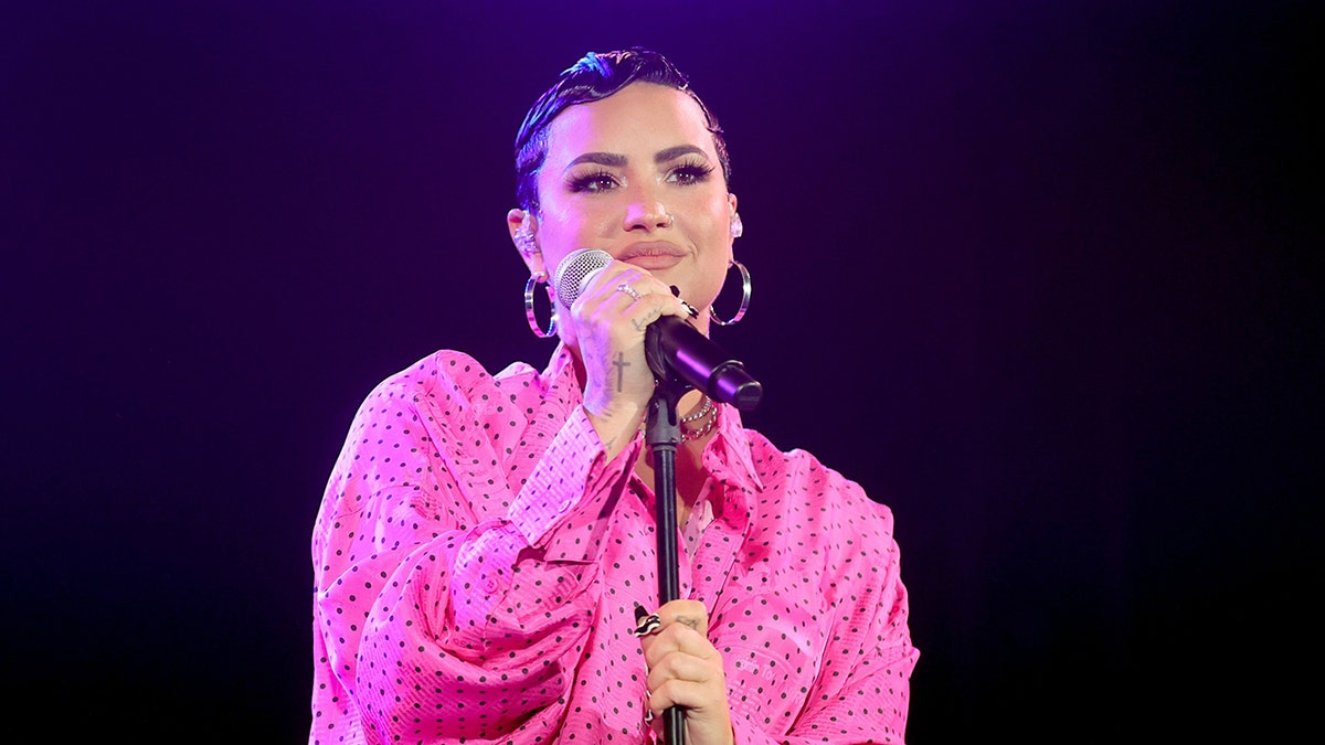 Demi Lovato singing in a bright pink shirt