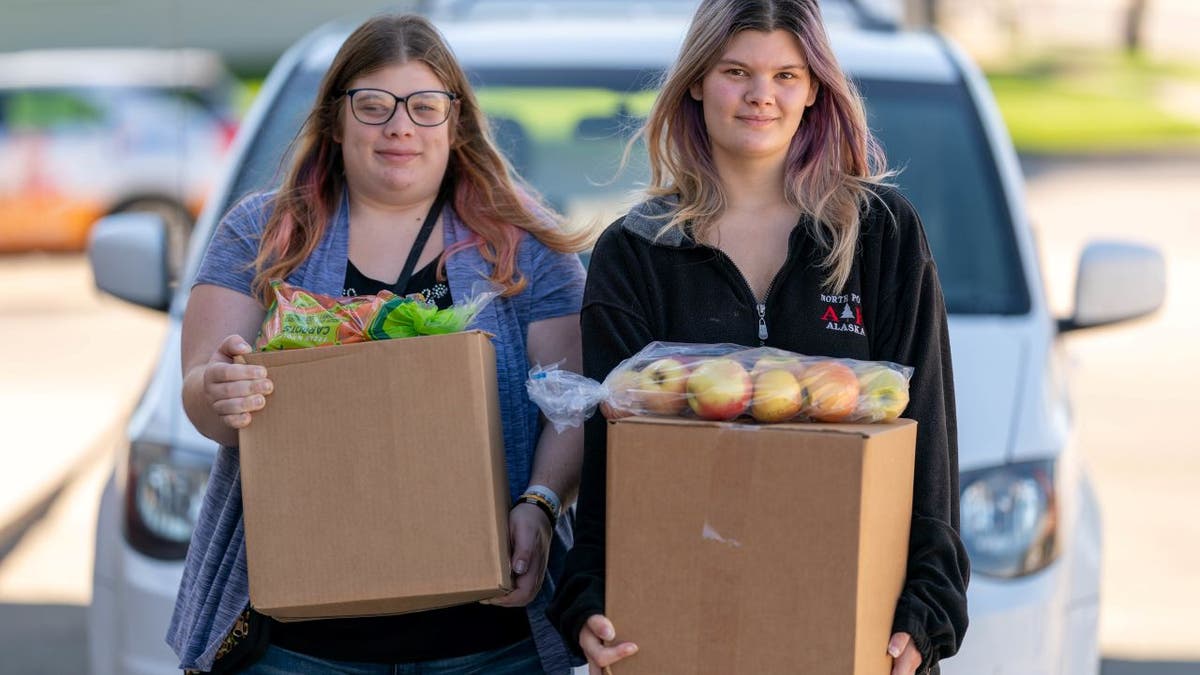 Two young women carry food in front of vehicles at a Feeding South Dakota location