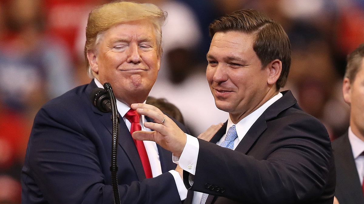Donald Trump and Ron DeSantis standing next to eachother at a podium, DeSantis speaking into the microphone