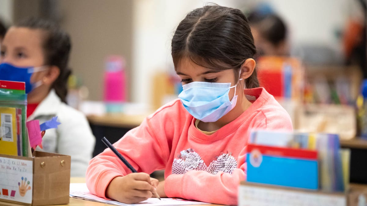 student wearing masks writes on paper