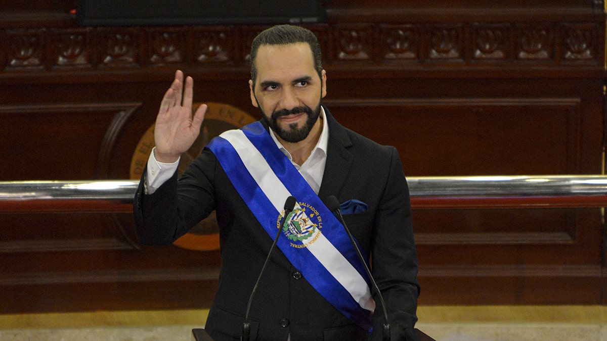 El Salvador President Nayib Bukele wears a black suit and a blue-and-white sash while waving to the crowd