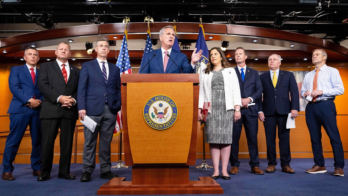 House Republicans stand in a briefing room with Kevin McCarthy at the podium