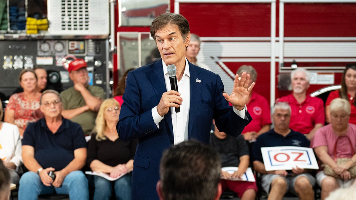 Dr. Mehmet Oz in a dark suit and white button holding a mic at a campaign event