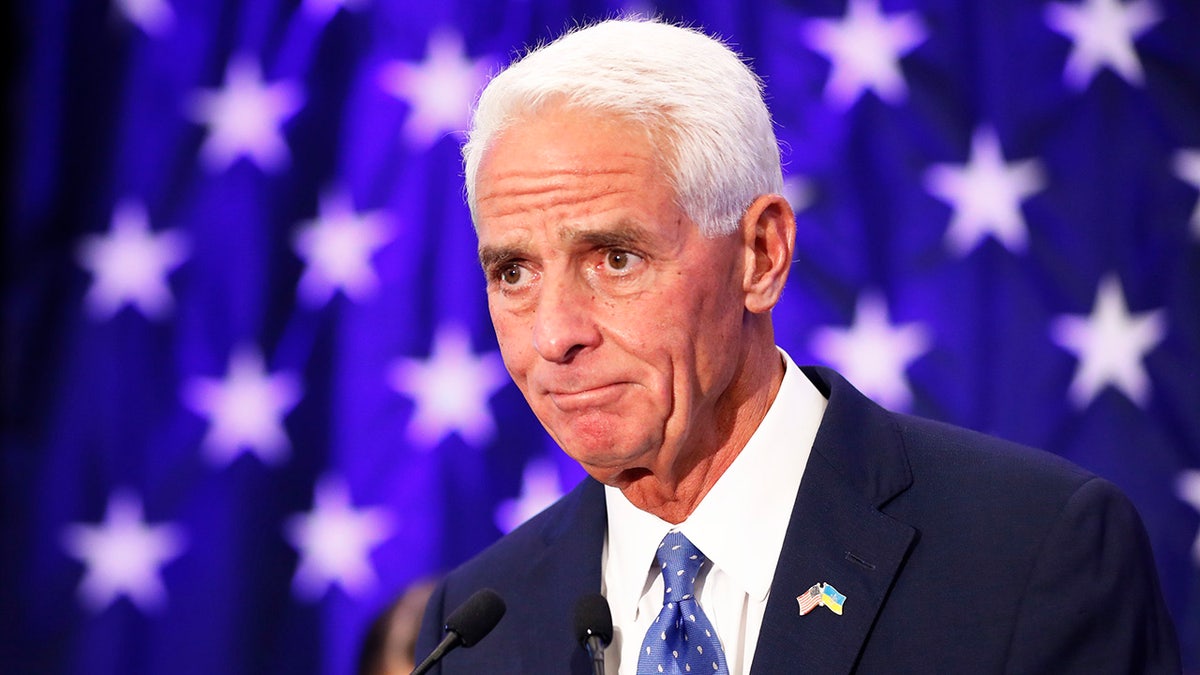Charlie Crist with a blue background and white stars, wearing a dark suit and blue tie