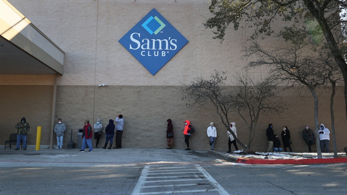 People line up outside a Sam's Club to social distance while wearing masks
