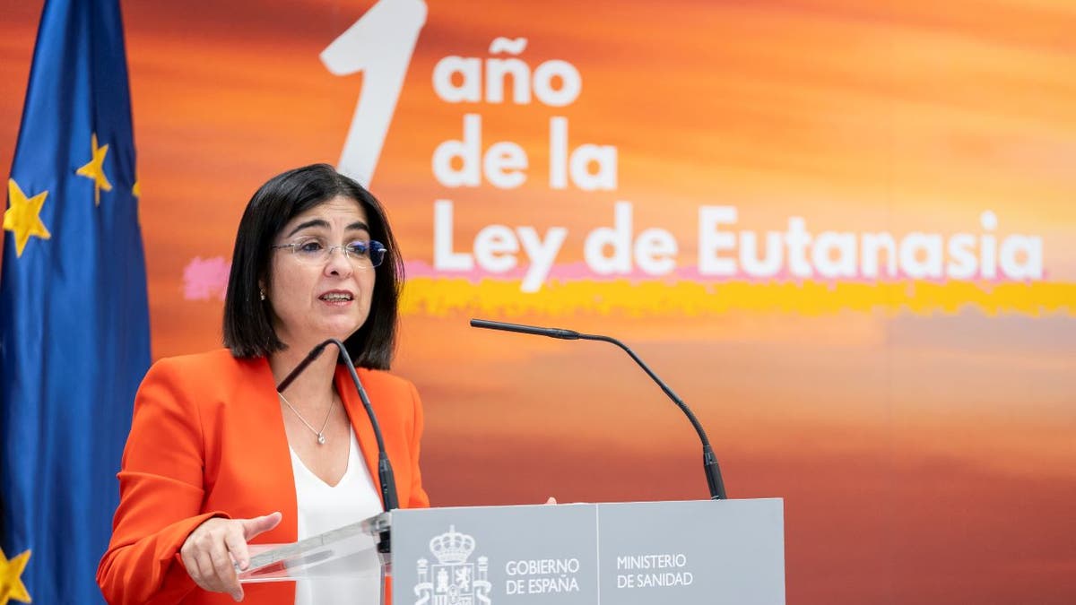 Spain Minister of Health speaks during press conference wearing orange jacket and white shirt