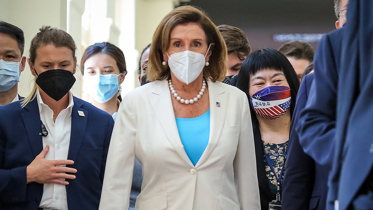 Pelosi walking down a hall in a facemask