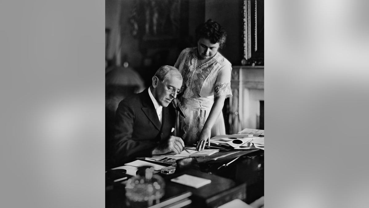 Woodrow Wilson (1856-1924), president from 1913-1921, goes over papers at his desk as his second wife Edith Bolling Galt Wilson looks on, mid 1910s. Edith was often referred to as "secret president" because of the important role she played in Wilson's presidency during his long and debilitating illness following a stroke.