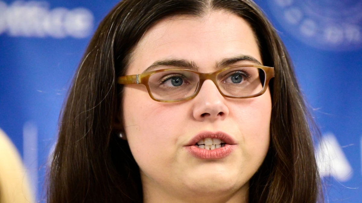 Jena Griswold speaking at news conference wearing green-rimmed eyeglasses