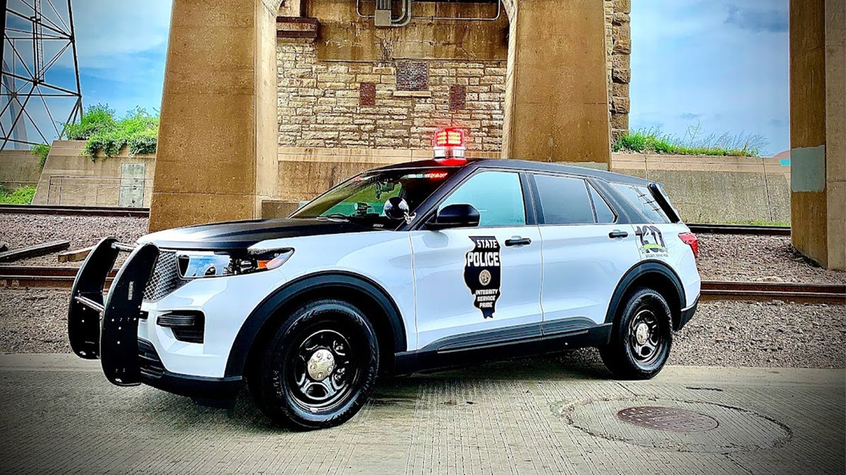 A black and white Illinois State Police cruiser is parked under a bridge