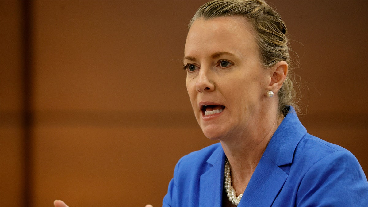 Melisa McNeill speaks, wearing a blue suit and a pearl necklace in a Fort Lauderale courthouse