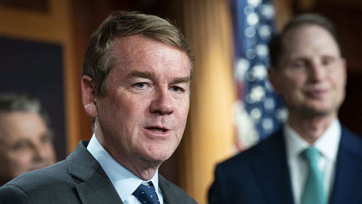 Sen. Michael Bennet in a grey suit with an American flag in the background