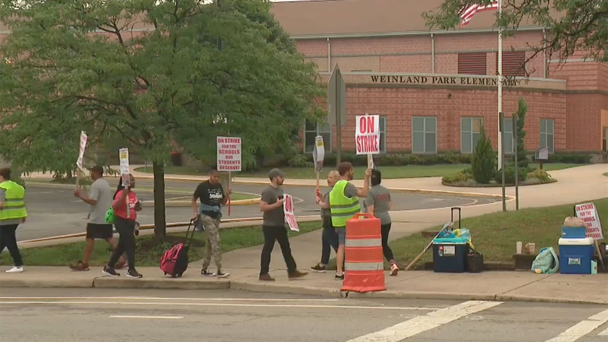 Teachers hold signs while marching outside of a school building