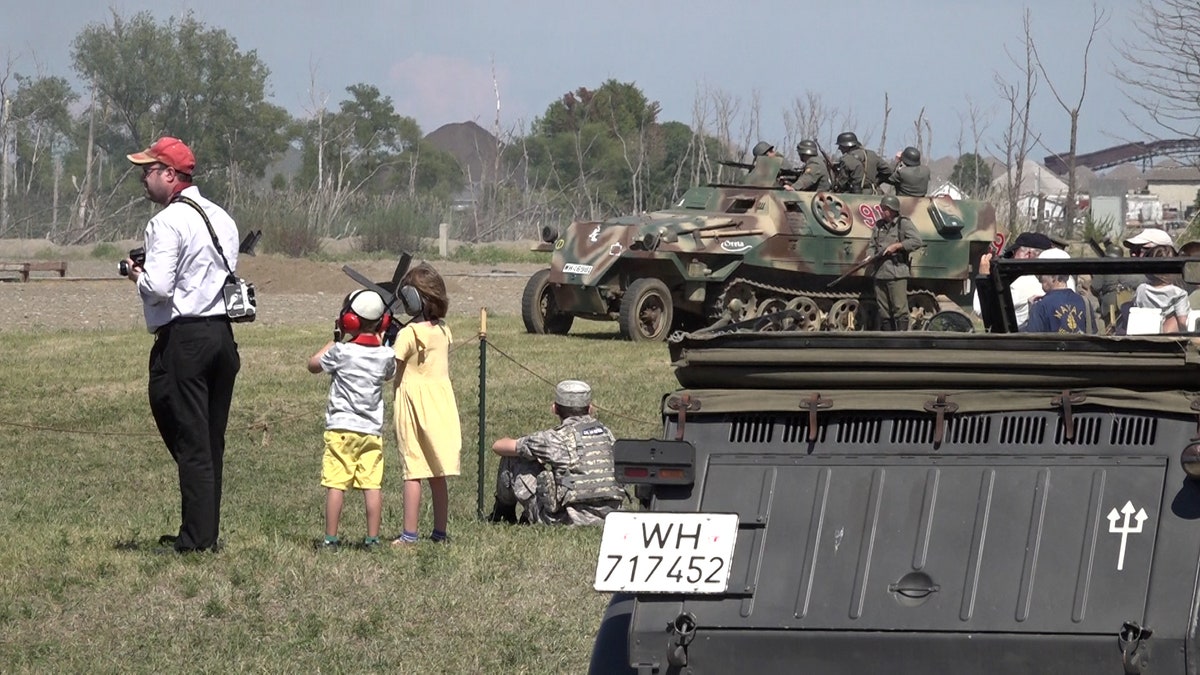 Man, two young children stands next to tank at World War II reenactment