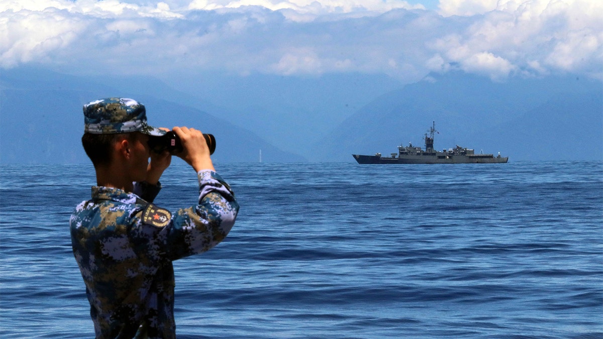 Chinesischer Soldat blickt durch ein Fernglas mit einem Militärschiff im Hintergrund
