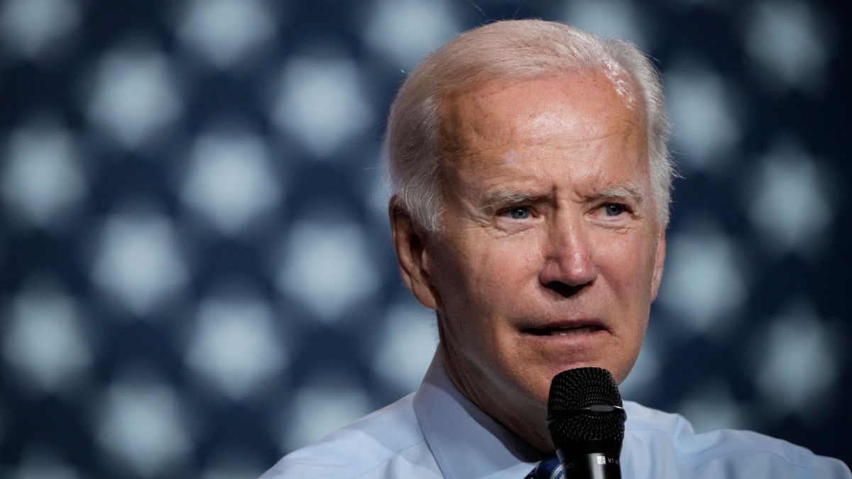 Joe Biden in a blue shirt with an American flag in the background speaks DNC rally